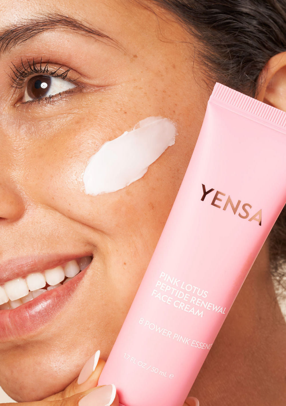 Close-up of a woman applying Pink Lotus Peptide Renewal Face Cream on her cheek for hydration and a healthy complexion.