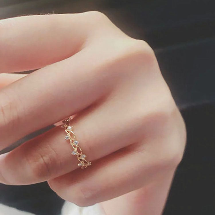 Close-up of a hand wearing a delicate gold ring with small stones on a blurred background