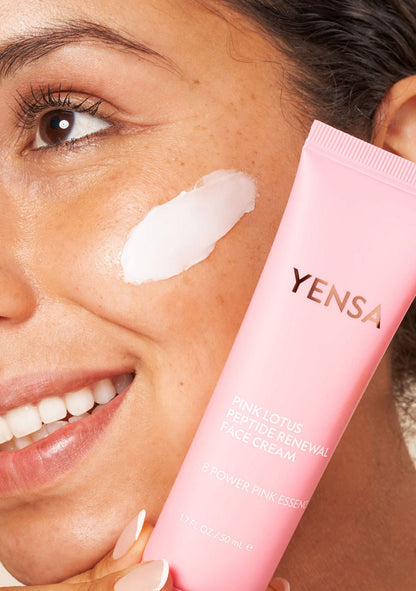 Close-up of a woman applying Pink Lotus Peptide Renewal Face Cream on her cheek for hydration and a healthy complexion.
