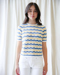 Woman wearing a blue and yellow patterned shirt against a white curtain background