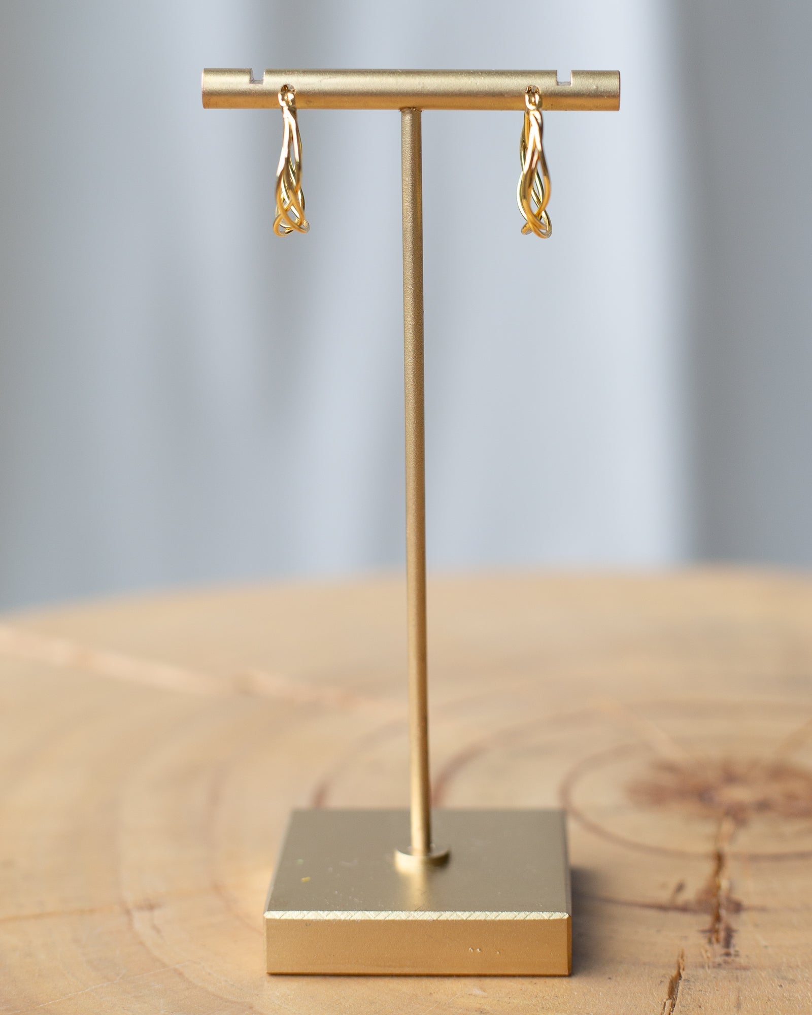 Braided Hoop Earrings displayed on a gold earring stand showcasing their elegant woven design.
